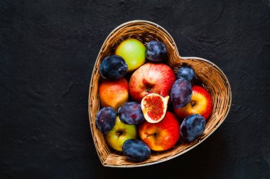 Sonbahar ev dekorasyonu. Kırmızı elma, Erik ve incir saman vazoda koyu mavi arka plan, üstten görünüm, organik gıda kavramı, detoks, üzerinde kalp şeklinde yapılan gıda veya vejetaryen kavramı temiz. Düz yatıyordu. 