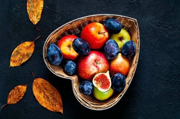 Röda äpplen, plommon och fikon i halm vas i form av hjärta på Mörkblå bakgrund, ovanifrån, ekologisk matkoncept, detox, ren mat eller vegetarisk koncept. Platt låg. Kopiera utrymme. — Stockfoto