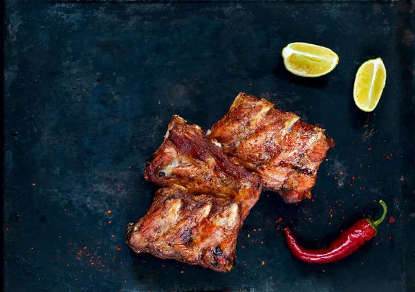 Costolette di ricambio piccanti alla griglia calde di barbecue servite con peperoncino piccante e lime su sfondo scuro. Bandiera. Vista dall'alto, spazio di copia, disposizione piatta . — Foto Stock