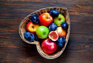 Elma, Erik ve incir ahşap arka plan, üstten görünüm, organik gıda kavramı üzerinde kalp şeklinde yapılan hasır vazoda,  