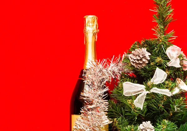 Блискучий різдвяний та новорічний декор. Декоративна ялинка зі срібною прикрасою та пляшка шампанського, прикрашена святковою тематикою на червоному тлі, крупним планом, місце для тексту — стокове фото