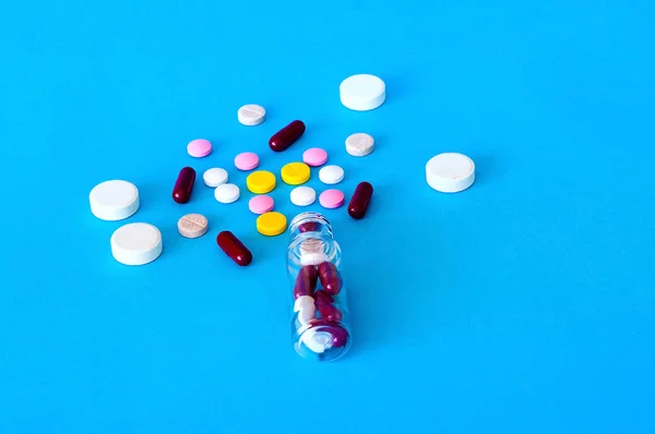 Цветные таблетки, капсулы, витамины, вылетающие из флакона на голубом фоне, концепция жизни, крупный план, копировальное пространство — стоковое фото