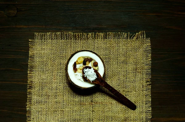 Vegetarischer Salat mit Kokosraspeln und Nüssen in Kokosnussschale auf der Textur von Klette auf Holzgrund. das Konzept der schmackhaften und gesunden Mahlzeit, Kopierraum, Nahaufnahme. — Stockfoto