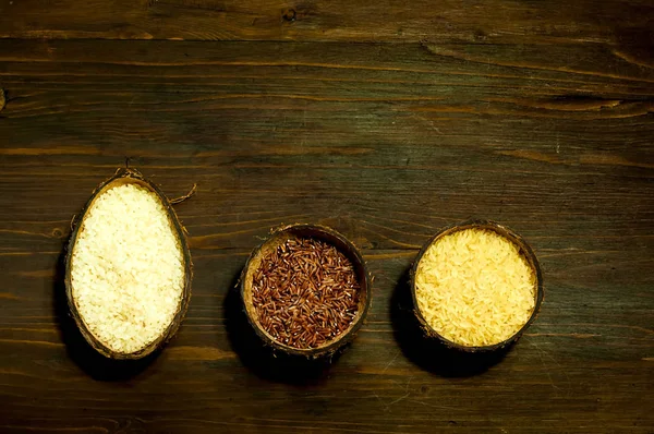 Verschillende soorten rijst in natuurlijke kokosnoot kommen op houten achtergrond. Het concept van smakelijke en gezonde maaltijd, kopie ruimte, close-up. — Stockfoto