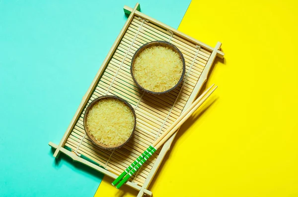 在有机椰子碗与筷子在几何纸背景上的大米。黄色和绿松石时尚的颜色, 关闭, 复制空间 — 图库照片