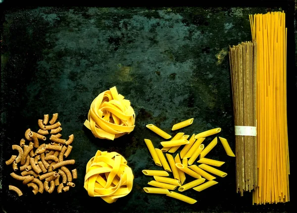 Verschiedene rohe Nudeln auf dunklem Hintergrund. Food-Konzept. flache Layeransicht mit Kopierraum. — Stockfoto