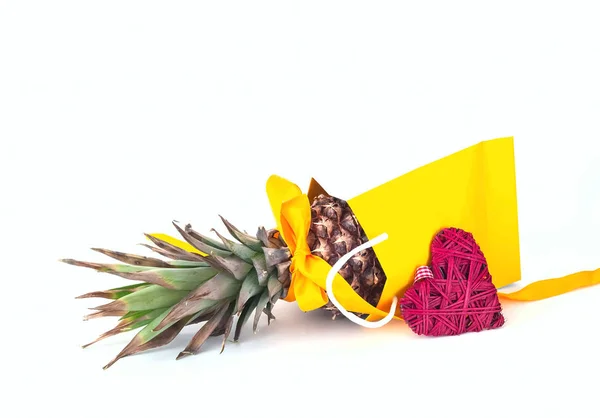 Pineapple with yellow ribbon in paper bag on white isolated background. Festive decor.