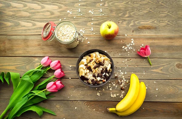 Colorful breakfast. Oatmeal with fruit and chocolate on a wooden background with tulips. — Stock Photo, Image
