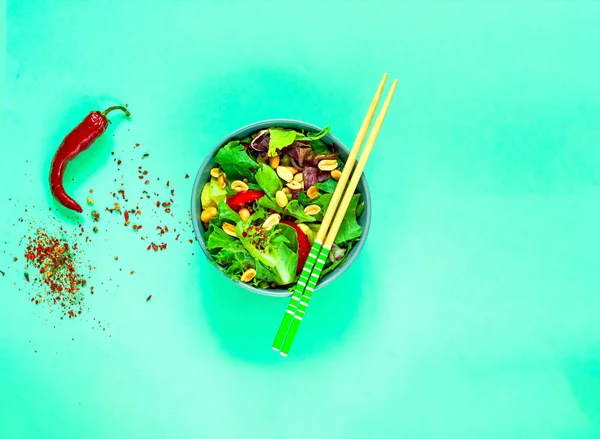 Vegan vegetabilisk sallad med jordnötter i blå skål med pinnar på grön bakgrund. Ekologisk matkoncept. — Stockfoto
