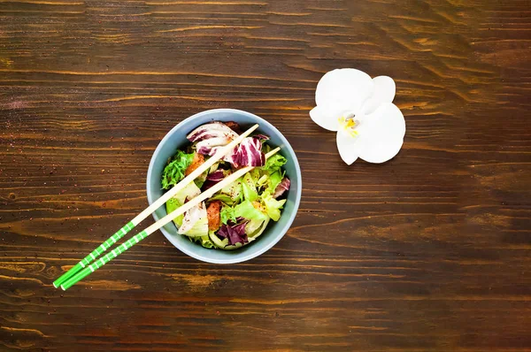 Салат из лосося в стеклянной чаше и палочки для еды на деревянном фоне . — стоковое фото