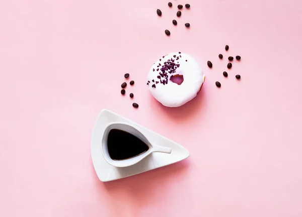 Színes reggelit. Csésze kávé és a fehér mázas fánk pasztell rózsaszín alapon fekete csokoládé édességek. — Stock Fotó