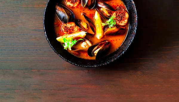 Mussels with sauce in authentic frying pan on wooden background.