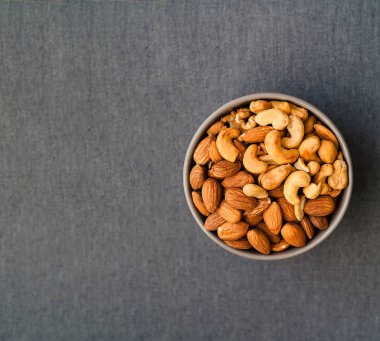 Sağlıklı kahvaltı. Gri arka planda mavi kasede cashews ve badem. 
