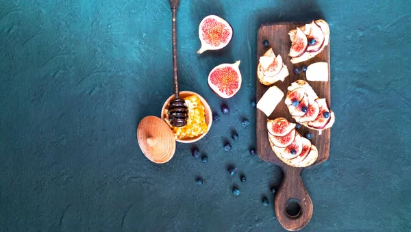 Sandwiches con higos frescos, queso de cabra, miel y arándanos sobre tabla de madera . — Foto de Stock