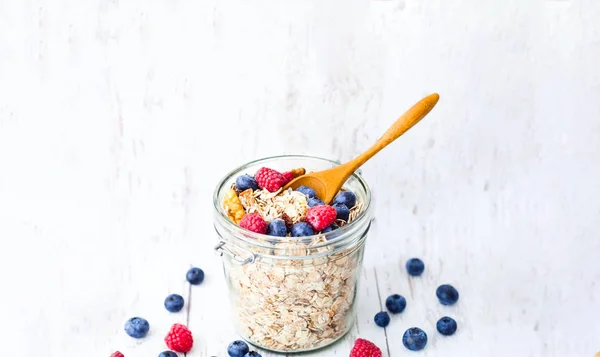 Muesli with blueberries and raspberries in glass jar on white wooden background. — Stock Photo, Image