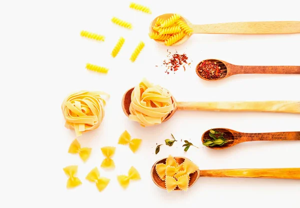 Trä skedar med pasta och kryddor på vit isolerad bakgrund — Stockfoto