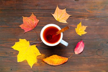 Ahşap arka plan üzerinde çay ve parlak turuncu yaprakları ile Fincan