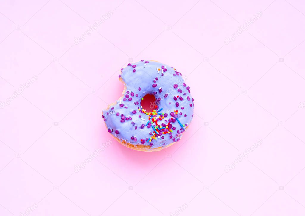 Eaten purple donut with colorful sprinkles on pink background. T