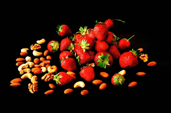 Reife Erdbeeren und verschiedene Nüsse auf dunklem Hintergrund. Gesundes E — Stockfoto