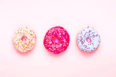 Renkli çörekler ve pembe arka planda rengarenk şekerler. Ulusal Pembe Gün veya Çörek Günü konsepti. 