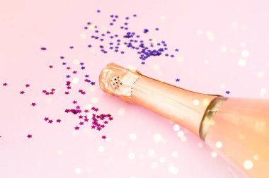 Pembe arka planda konfeti olan şampanya şişesi. Bulanık etki. Noel tasarımı için yaratıcı alan. 