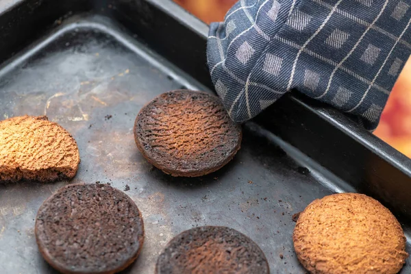 Burnt cookies. A hand in a oven glove, potholder picks up a black baking tray with burnt cookies