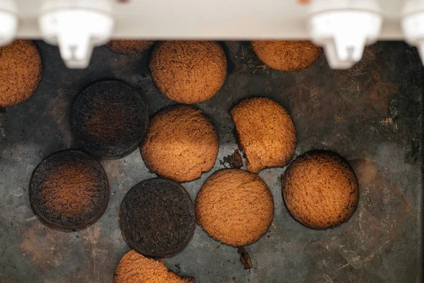 Burnt cookies. Burnt, burnt oatmeal cookies lie on a black baking sheet. Vertical photo