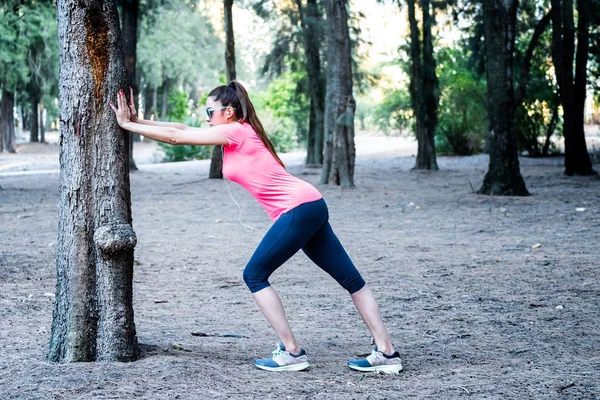 Mujer blanca que se extiende sobre un árbol en un parque — Foto de Stock