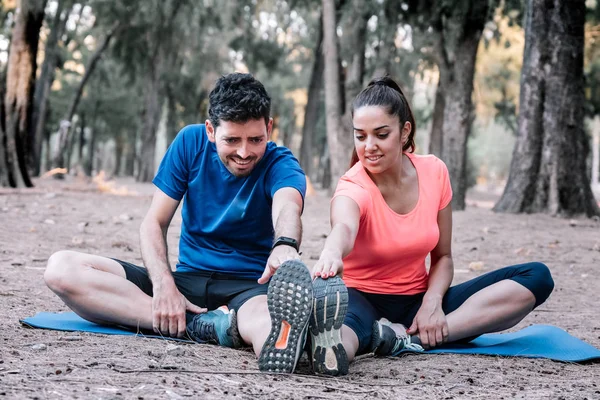 bir parkta oturan çift germe egzersizleri yapıyor