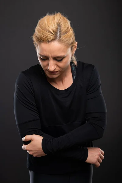 Portrait of gym female trainer holding elbow like hurting on black background