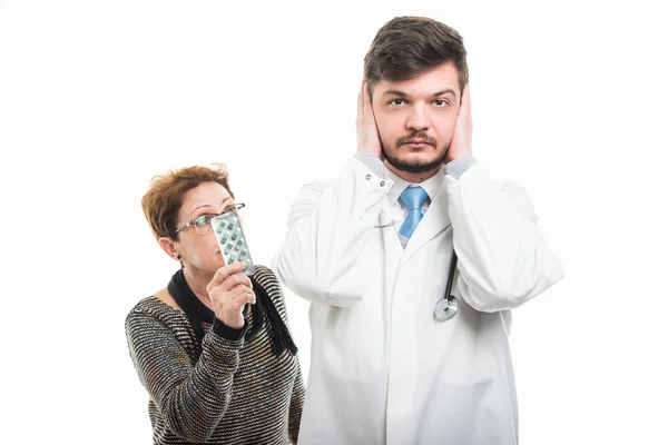 Lékař Pokrývající Uši Pacientka Ukazující Prášky Izolovaných Bílém Pozadí — Stock fotografie