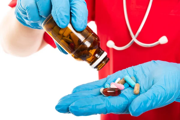 Copyspace 折込広告エリアで白い背景に分離された薬の瓶をこぼれる赤のスクラブを着ている若い医療看護師のクローズ アップ — ストック写真