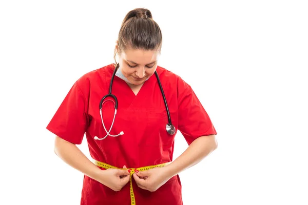 Copyspace 折込広告エリアで白い背景に分離されて腰を測定赤いスクラブを着て若い医療看護師の肖像 — ストック写真