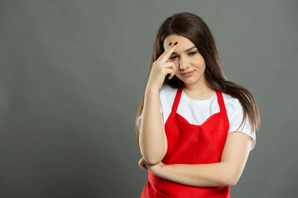 Portrait of young female supermarket employee making thinking gesture on gray background with copy space advertising area