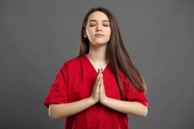 Genç esmer hemşire, gri bir arka planda kırmızı önlük giyerek Tanrı 'ya oyun oynuyor.