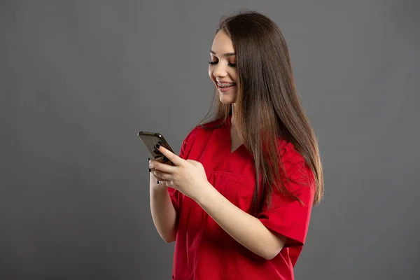 Young Brunette Nurse Browsing Internet Her Phone Wearing Red Hospital — Stock Photo, Image