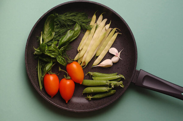 organic fresh vegetables courgette, tomato, asparagus, basil, dill, green peas, garlic in a frying pan