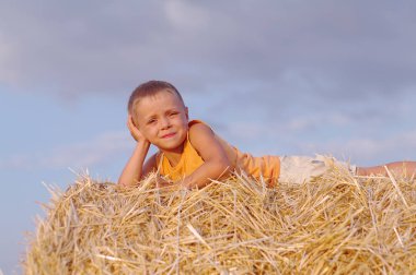 Buğday tarlası samanlıkta oturan bir yaz şapkalı küçük çocuk portresi. Güzel gün batımı