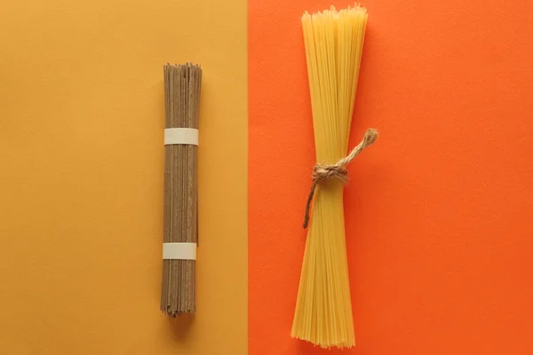 Buchweizen-Nudelspaghetti und Vollkornspaghetti auf leuchtend gelb-orangefarbenem Hintergrund. Ansicht von oben. Text platzieren — Stockfoto