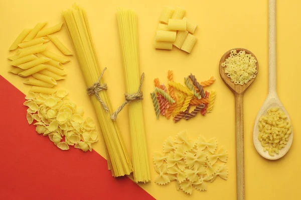 Verschiedene Arten trockener Pasta: Spaghetti, Penne, Farfalle, Tagliatelle, Fettuccine auf leuchtend gelb-rotem Hintergrund.. — Stockfoto