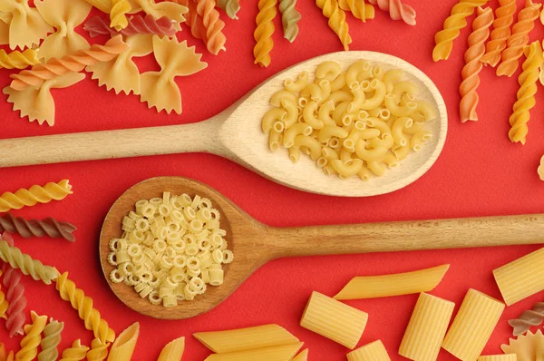 Verschiedene Arten trockener Pasta: Spaghetti, Penne, Farfalle, Tagliatelle, Fettuccine auf leuchtend rotem Hintergrund.. — Stockfoto