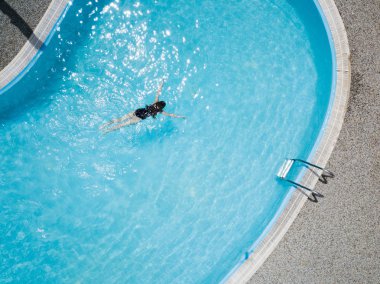 Bir genç kızın Siyah mayo, mavi yüzme havuzu ve beyaz şezlong havadan görünümü