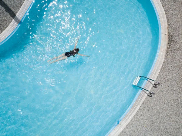 Aerial image about a blue swimming pool outdoor, a girl enjoys the water sport activity.