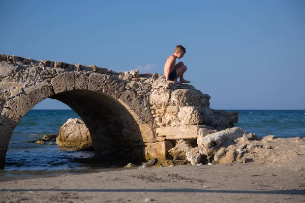 Ragazzino Gioca Vecchio Ponte Pietra Rovina Accanto Una Spiaggia — Foto Stock