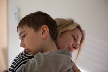 Sarışın anne ve esmer çocuk birbirlerine sıcak sarılmak. Kapalı, doğal ışık.