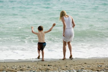 Sarışın ince anne ve çocuğu birlikte yaz zevk, plajda deniz dalgaları.