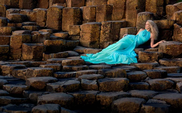 北アイルランドのジャイアンツコーズウェイでターコイズロングドレスの美しいブロンドの女性 — ストック写真