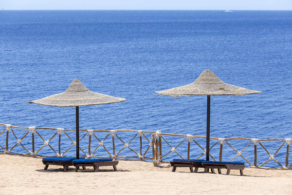 Two beach straw umbrellas with wooden sun loungers next to the red sea at the resort in Sharm El Sheikh, Egypt