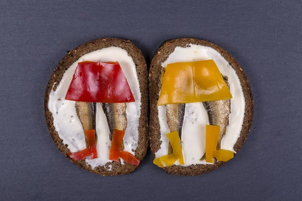 Funny food, sandwich with red and yellow pepper, sprats and soft cheese on the background of black slate , close up, top view