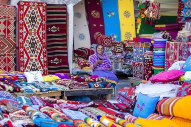 Doha, Katar - 25 Aralık 2017: Multicolour halı, kilim ve diğer öğeleri ile Doha, Souq Waqif pazarı, kadın tüccarı. Doha, Qatar